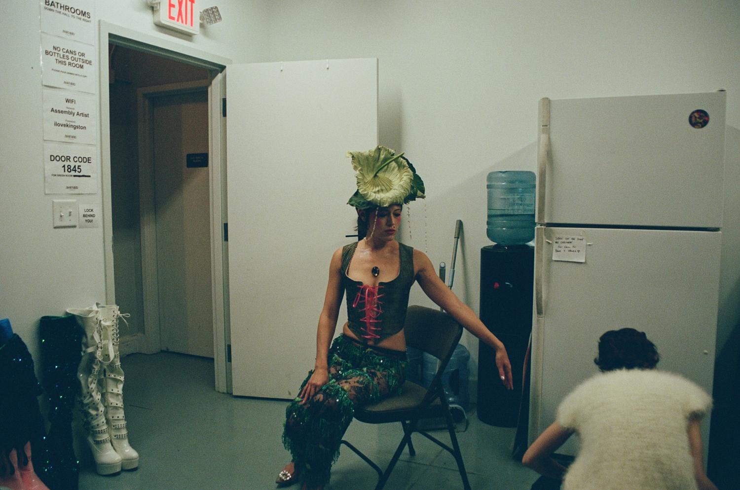 A performer in a leaf headdress resting backstage