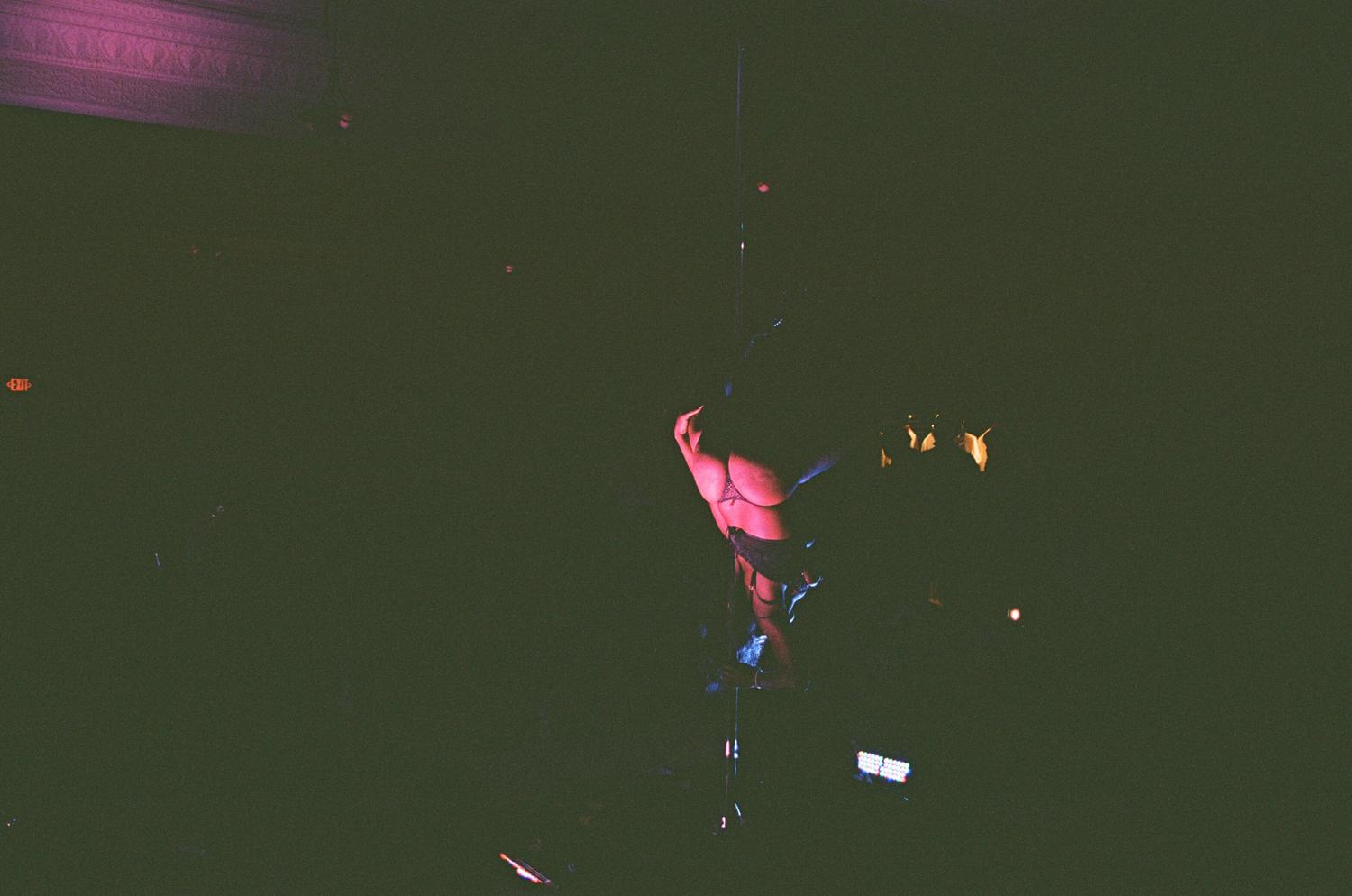 A dancer on the pole, lit pink in a dark room